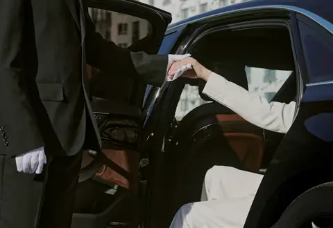 A chauffeur in white gloves helps a female passenger out of a luxury car