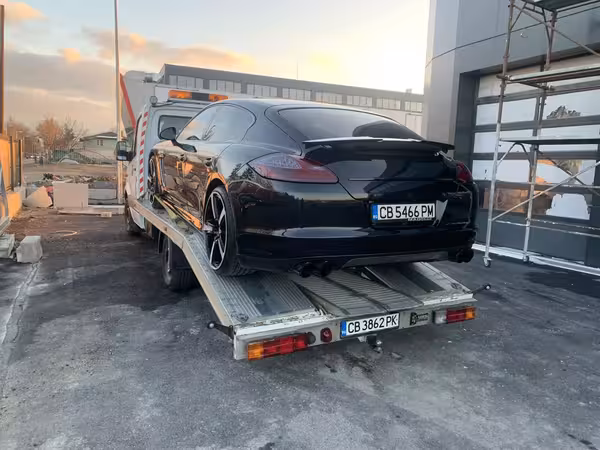 Черен спортен автомобил на платформа на репатрак пред сервиз, пътна помощ и извозване на автомобил